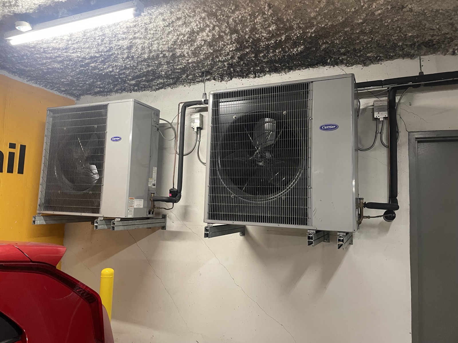Two Carrier commercial condenser units mounted on a parkade wall during an HVAC replacement